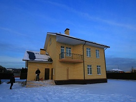 снег на крыше кирпичного двухэтажного дома под съем с балконом и крыльцом со ступенями на зимнем участке