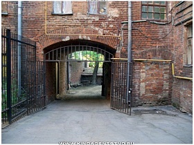 металические ворота из черных прутьев в арочном переходе старого кирпичного трехэтажного дома