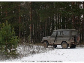 машина УАЗ на дороге под снегом на вьезде в густой смешанный лес