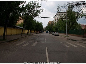 автомобильная двухполосная дорога с пешеходной зеброй вдоль желтого забора института классического советского образца 80 годов