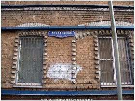 синяя вывеска на кирпичной стене между окнами с решетками старого трехэтажного дома