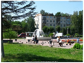 дети на велосипедах, мамочки на скамейках в городском небольшом парке отдыха с фонтаном в  Ивантеевке