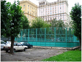 детская спортивная площадка за забором с зеленой сеткой во дворе сталинского здания