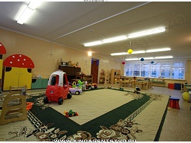 яркие разноцветные атрибуты, детские машины на большом ковре игровой зоны детского сада