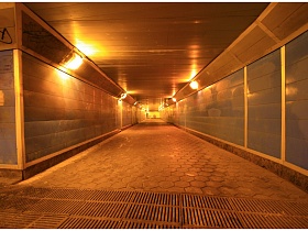 длинный подземный переход Советского типа с серой плиткой на стенах и шестигранной плиткой на полу