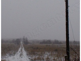 деревянный столб с линией электропередач у дороги на пустыре под снегом, уходящей в зимний лес