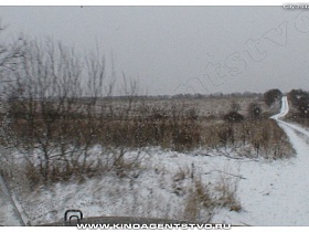 извилистая проселочная накатанная заснеженная дорога в чистом просторном поле с заросшей травой под белым снегом