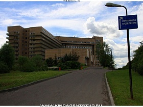 указатель на высоком осветительном столбе вдоль дороги со шлагбаумом на вьезде к корпусу многоэтажного здания большой больницы