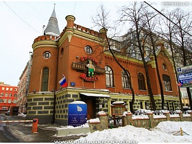 яркая красочная вывеска паба с названием и изображением старины Мюллера на кирпичного цвета здании на высоком фундаменте в готическом стиле, с башней, арочными окнами и конусообразной крышей