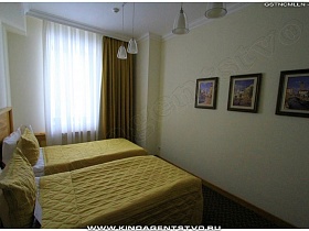 две односпальные кровати с желтыми стеганными покрывалами у деревянной спинки в спальне гостиничного номера