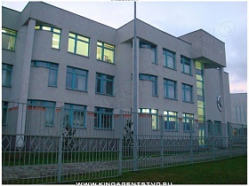 трехэтажное серое здание школы-гимназии за белым металлическим забором