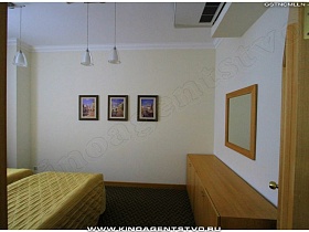 картины на стене и зеркало в деревянной рамке над деревянной длинной тумбой в спальне номера высотного отеля