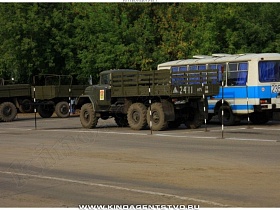 грузовые автомтбили защитного цвета и автобус на площадке за ограждением при автошколе