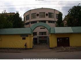 зеленая арка над железными воротами и зеленая крыша над стенами желтого забора у центрального входа на территорию института классического советского образца 80 годов с круглым спортзалом