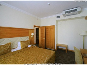 встроенный деревянный шкаф и скамеечка у стены с кондиционером в спальне номера высотного отеля