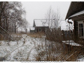 заснеженные крыши старых неокрашенных деревянных домов с покосившемся забором вдоль улицы в зимнее время
