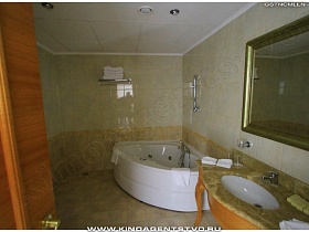 угловая ванна и зеркало в деревянной рамке над раковиной на фигурных ножках в ванной комнате гостиничного номера