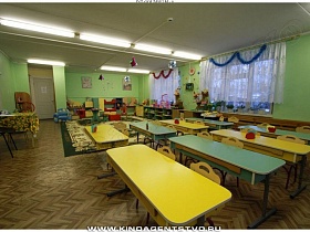 желтые и зеленые деревянные столы и стульчики в просторной комнате для приема пищи в детском саду