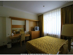 желтые шторы на окне и желтое стеганное покрывало на большой кровати с подушками в спальне номера высотного отеля