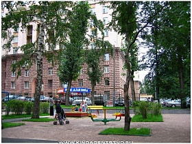 яркая игровая детская площадка за высоким забором во дворе сталинского дома