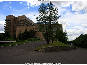 шлагбаум на въезде дороги к высокому корпусу большой больницы на холме в окружении высоких зеленых елей и лиственных деревьев