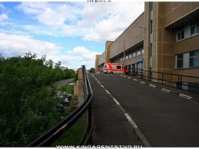 асфальтированная дорога с металлическим ограждением, пешеходной дорожкой для служебного трансполрта к приемному отделению главного корпуса большой многоэтажной больницы