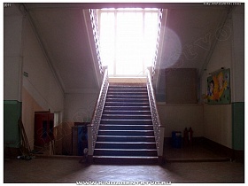 уголок пожарника с инвентарем и ярким стендом у лестницы с перилами на верхние этажи общеобразовательной  школы №1