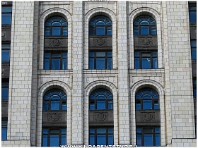 фасад белого высотного здания с арочными окнами в стиле сталинский ампир во дворе с полисадником у Москвы реки