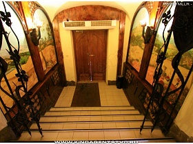 черные кованые элементы декора на ступенях, выложенных плиткой, бра под старину на стенах с красочным арочным пано в коридоре на выходе из паб ресторана в немецком стиле