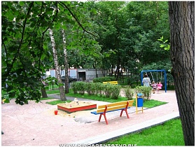 разноцветные песочница, качели и скамейки на детской площадке во дворе сталинского дома