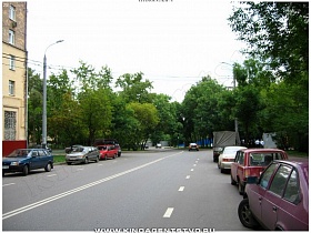 автомобильная дорога с припаркованными машинами вдоль сталинского здания