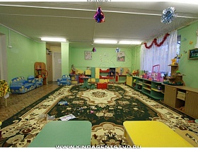 мягкие диванчики и кресла, столики, шкафы с полочками для игрушек в светлой просторной игровой комнате детского сада