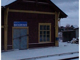 синяя вывеска магазина над закрытыми железными дверьми в одноэтажном коричневом здании на железнодорожной станции Калашниково