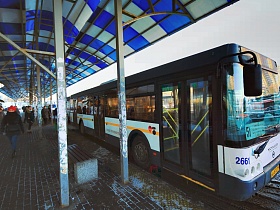 деревянные окрашенные скамейки на бетонных стойках на длинной автобусной остановке с пассажирскими автобусами на посадке