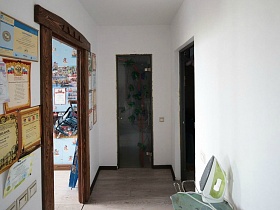 дипломы и грамоты на стене у двери с деревянной резной луткой в белой прихожей семейной трехкомнатной квартиры