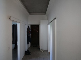 настенная вешалка с одеждой, белый шкаф, обувь на пороге прихожей с белыми стенами, серым полом и потолком современной скандинавской квартиры