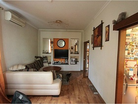 круглые часы и плоский телевизор внутри белой стенки из гтпсокартона в гостиной трехкомнатной  семейной квартиры в сталинке