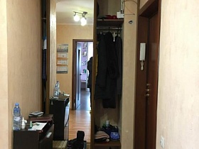 коричневый шкаф-купе с зеркальными дверцами, коричневый шкаф для обуви, деревянный стул, обувь на коврике у входной двери в прихожую с бежевыми обоями на стенах