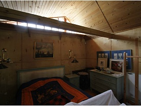 картины в рамках на белом комоде у кровати с прикраватной тумбочкой в спальной зоне деревянного домика на дачном участке