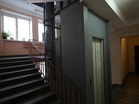 бетонные ступени лестницы с перилами в подъезде с комнатными цветами на подоконниках и лифтовой кабиной за металлической сеткой