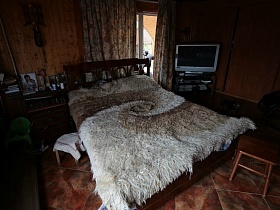фотографии на прикроватной тумбочке,деревянная кровать с меховым светлым покрывалом, телевизор на тумбе в углу спальной комнаты классической семейной дачи