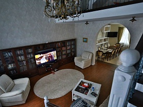 общий вид гостиной и столовой через арочный дверной проем с высоты лестницы добротного современного кирпичного дома