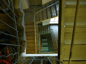 вид сверху на бетонные ступени лестничных пролетов винтовой лестницы в сером подъезде жилого многоэтажного дома эпохи СССР