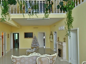 яркая сочная зелень комнатных растений за белыми перилами второго этажа над светлой гостиной яркого дизайнерского дачного дома в густом сосновом лесу