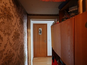 указатель с картинкой на деревянной двери санузла в светлом коридоре из прихожей со старыми обоями и мебелью советского времени