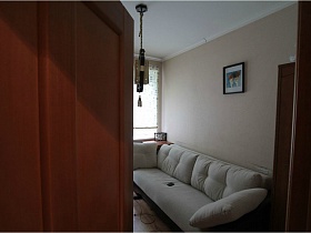 белый диван с мягкими подушками у стены светлой комнаты в трешке сталинского двора