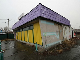 продуктовый магазин в одноэтажном здании, требующего ремонта с сиреневой крышей и ярко желтым фасадом в сельской местности