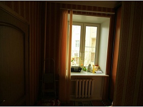желтые вертикальные жалюзи на окне со шкатулкой, утюгом, желтым пулевизатором на белом подоконнике прихожей с яркими полосатыми обоями на стенах стильной квартиры