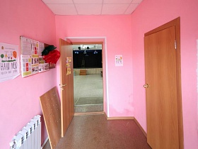 ухоженный чистый длинный коридор с информацией на стенде на розовых стенах и открытой дверью в большой зал сельского театра
