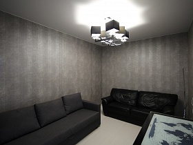 карта мира на черном столике, два дивана с подушками у серых полосатых стен комнаты для гостей современной трехкомнатной квартиры в стиле хай-тек